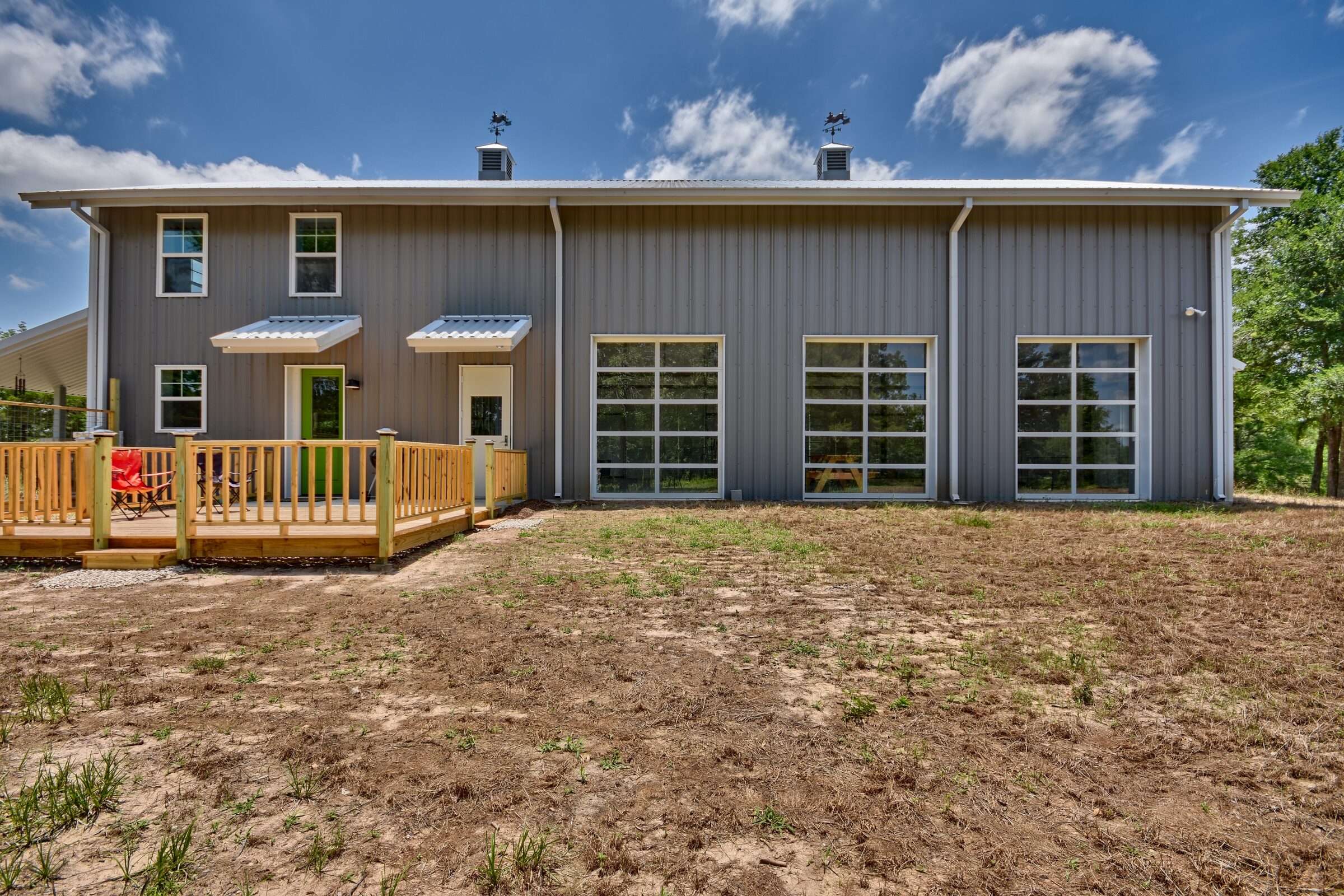 Rear elevation of the barndominium with a timber deck, awnings over the entries and three tall multi-light windows