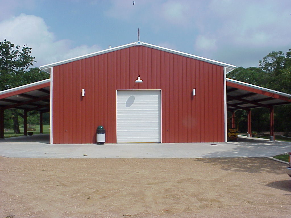 Straight-on view of the party barn end wall showing the overhead door and the lean-to roof dropped below the main roofline on both sides