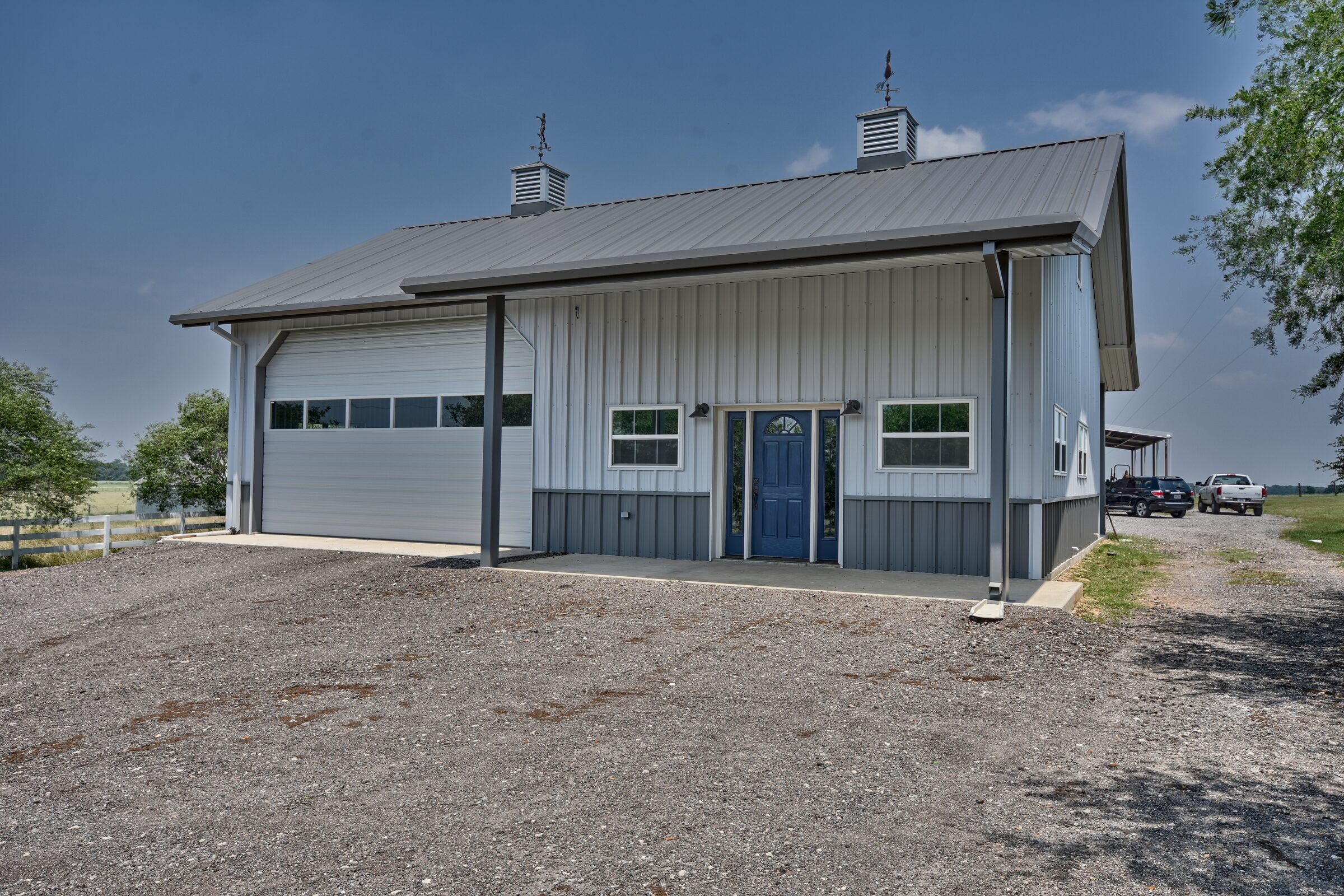 Three-quarter view of a white and grey metal shop building with an oversized roll-up door, covered porch and blue entry door