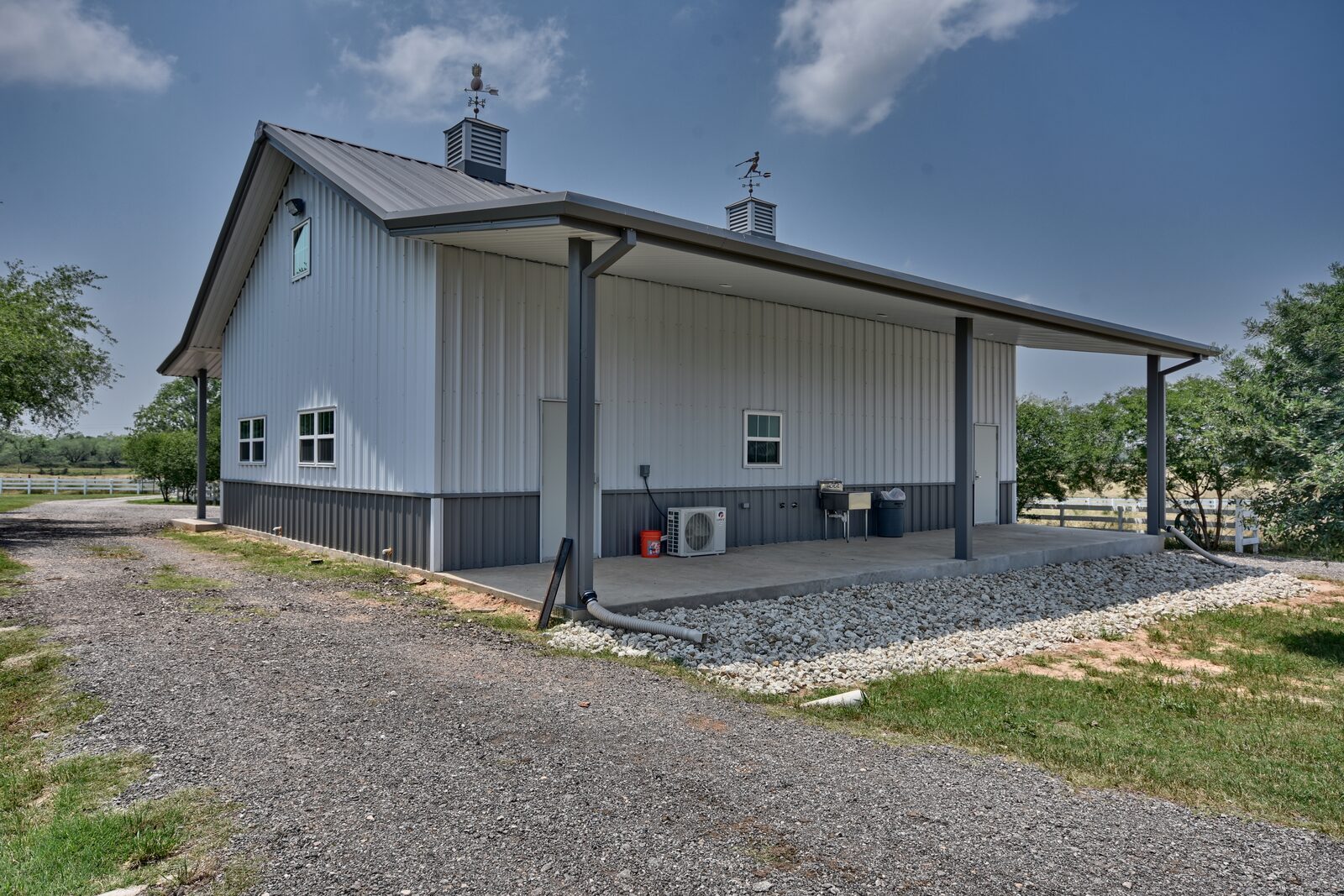 Covered porch running along the side of a metal shop building, with a walk door and mini-split unit
