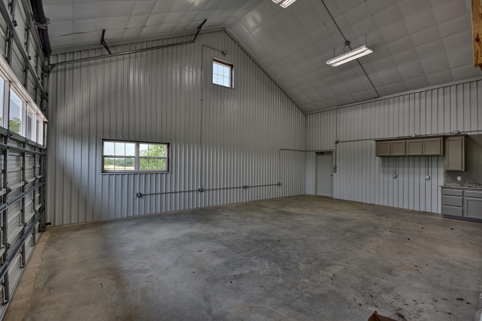 Empty shop interior with vaulted ceiling, windows, a walk door and wall cabinets with a granite counter