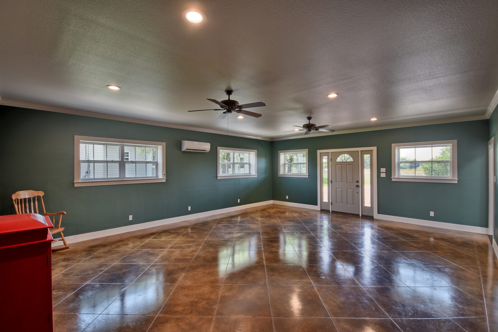 Finished room with deep green walls, stained and scored concrete floor, ceiling fans and the front entry door