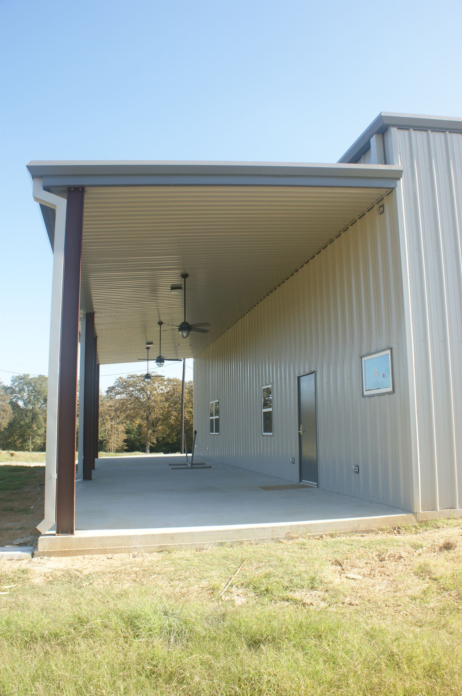 Covered porch along a Rhodes Building Systems shop building with ceiling fans, windows and a walk door